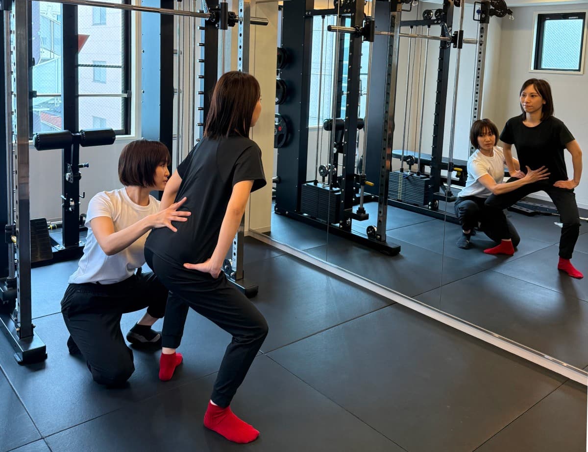 トレーナーが姿勢を見ながらスクワットを指導する様子